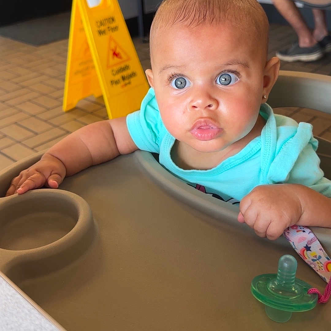 Leilanii joined the competition — help win amazing prizes! baby, blue_eyes, casual, caution_sign, child, clothing, expression, face, floor_sign, furniture, hand, high_chair, indoor, pacifier, people, person, restaurant, seat, skin, table