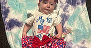 Lainey is registered to the contest to win money with this photo: baby, infant, blanket, headband, bow, red, white, blue, clothing, foot, toenails, carpet, person, lying_down, pattern, cute, soft_texture, patriotic, shoes, toddler