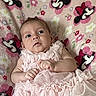 baby, infant, pink_dress, blanket, minnie_mouse, pattern, cute, face, person, child, lying_down, soft_texture, fabric, clothing, indoor, portrait, expression, hands, young, toddler