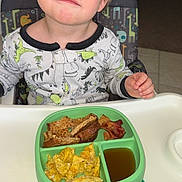 Leo joined the competition — help win amazing prizes! toddler, child, high_chair, pajamas, dinosaur_print, scrambled_eggs, toast, bacon, syrup, plate, green_plate, indoor, kitchen, food, meal, breakfast, person, blue_eyes, blonde_hair, expression