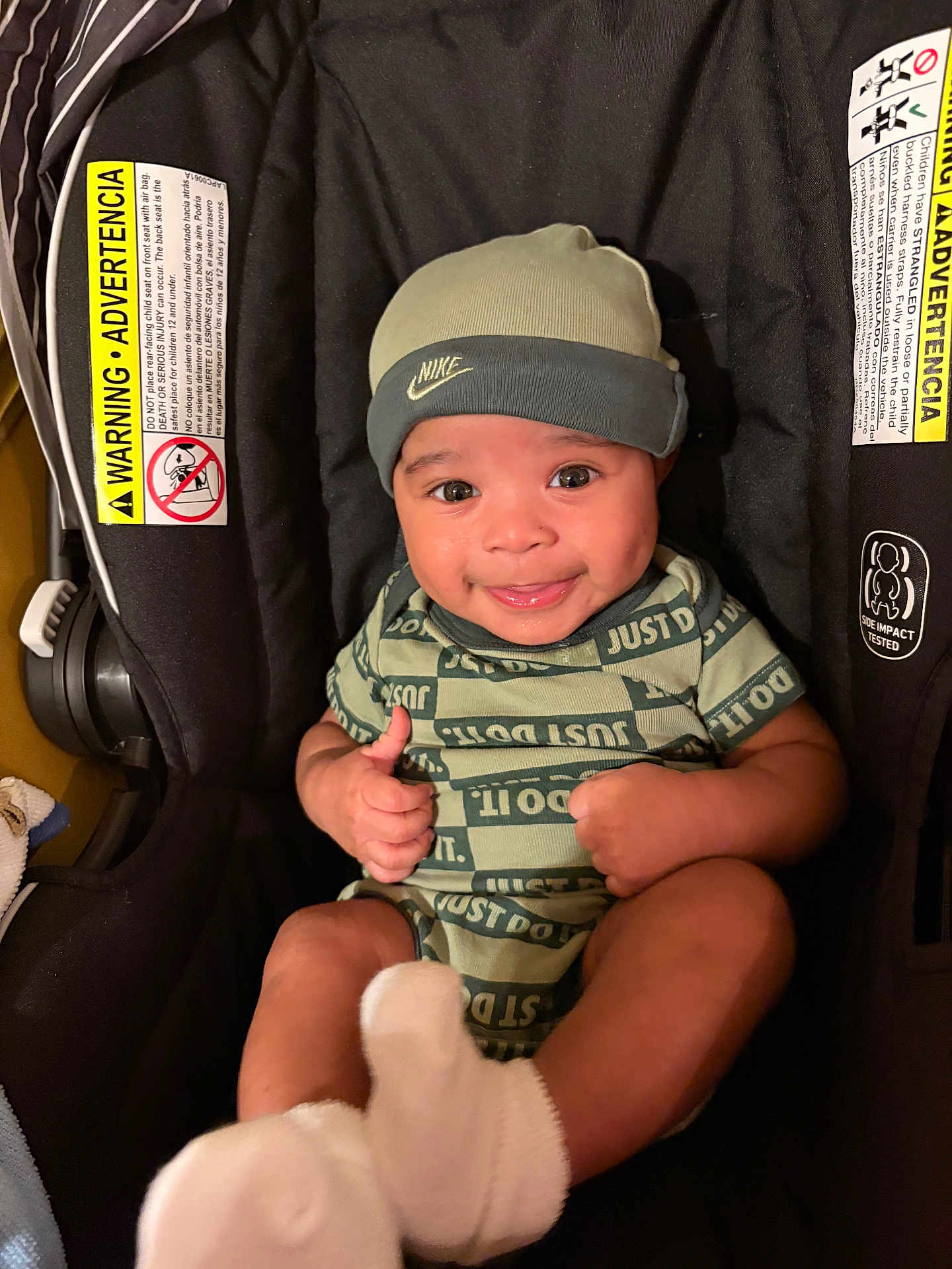 Pablo is registered to the contest to win money with this photo: baby, infant, smiling, thumbs_up, car_seat, nike, beanie, green_clothing, socks, happy, cute, child, portrait, indoors, person, infant_clothing, infant_accessories, seat, sitting, apparel