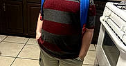 James is registered to the contest to win money with this photo: child, boy, portrait, standing, backpack, kitchen, stove, cereal_box, countertop, cabinets, sink, floor_tiles, striped_shirt, shorts, sneakers, indoors, home, looking_up, full_body, smiling