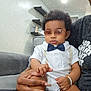 baby, child, sunglasses, bow_tie, white_outfit, hand, manicure, living_room, couch, sitting, adult, modern_interior, shelf, light, calm, fashion, portrait, indoor, sparkle_filter, skin