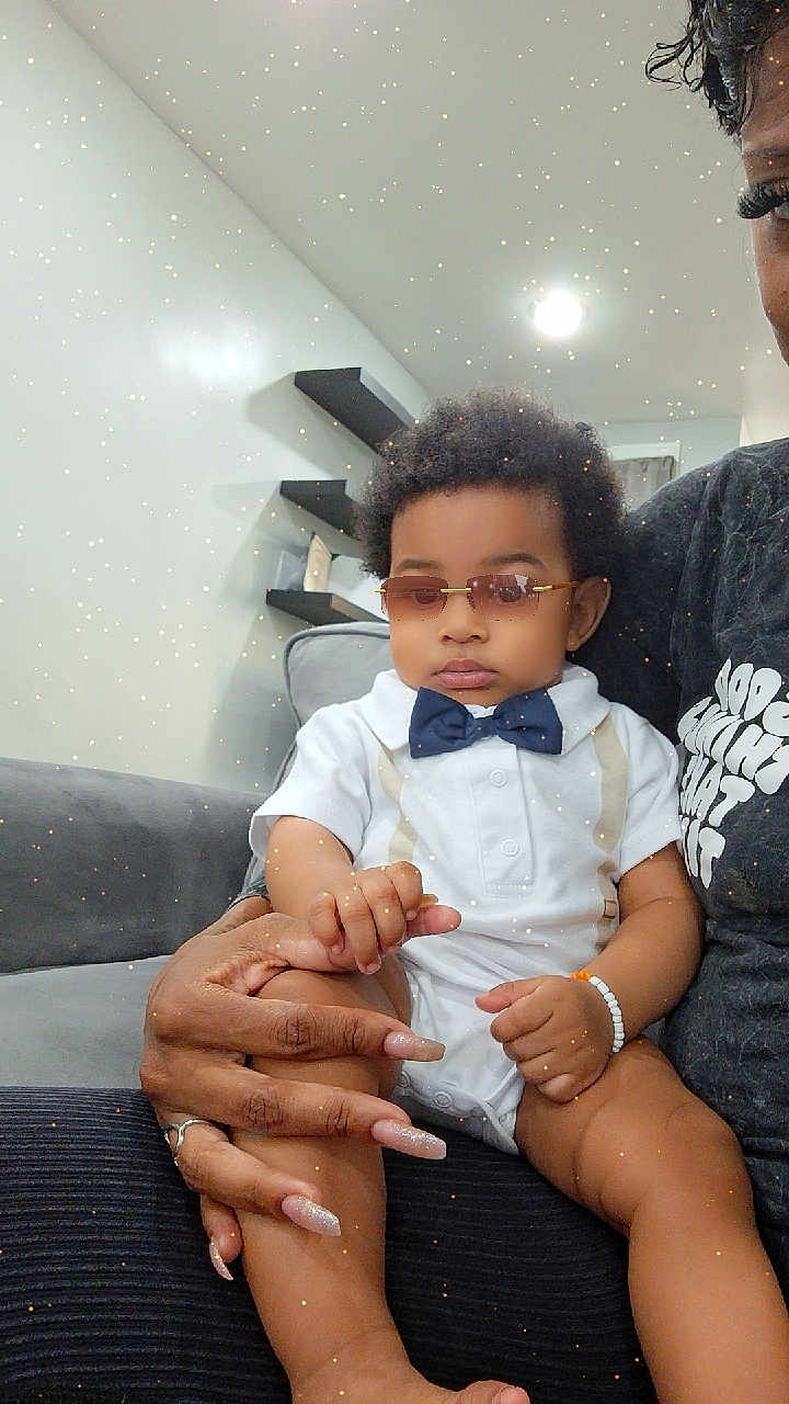 Jonas joined the competition — help win amazing prizes! baby, child, sunglasses, bow_tie, white_outfit, hand, manicure, living_room, couch, sitting, adult, modern_interior, shelf, light, calm, fashion, portrait, indoor, sparkle_filter, skin