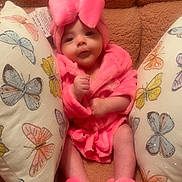 Delylah Rose is registered to the contest to win money with this photo: baby, infant, pink_clothing, robe, slippers, couch, pillows, butterfly_pattern, soft_texture, cozy, indoor, child, cute, portrait, smiling, comfortable, fluffy, headwear, home, sparkles