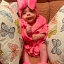 baby, infant, pink_clothing, robe, slippers, couch, pillows, butterfly_pattern, soft_texture, cozy, indoor, child, cute, portrait, smiling, comfortable, fluffy, headwear, home, sparkles