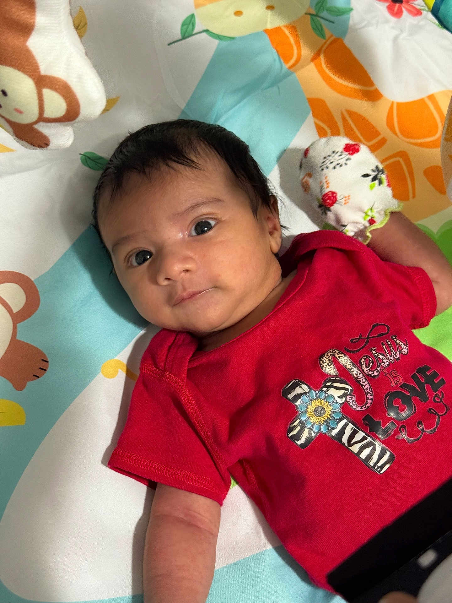 John joined the competition — help win amazing prizes! baby, infant, face, red_shirt, mitten, playmat, monkey_pattern, colorful, cute, child, apparel, handwear, lying_down, portrait, young, skin, hair, expression, indoors, resting