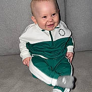 Thibault a rejoint le concours — aidez-le/la à gagner de superbes lots ! baby, child, smiling, couch, gray_couch, tracksuit, green_clothing, white_clothing, socks, nike_socks, indoor, home, seated, cute, happy, infant, person, face, footwear, furniture
