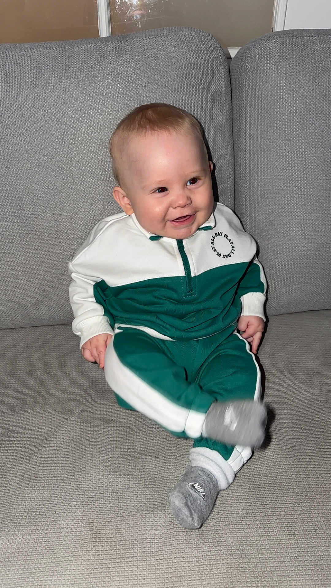 Thibault a rejoint le concours — aidez-le/la à gagner de superbes lots ! baby, child, smiling, couch, gray_couch, tracksuit, green_clothing, white_clothing, socks, nike_socks, indoor, home, seated, cute, happy, infant, person, face, footwear, furniture