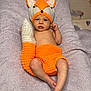 baby, newborn, infant, fox_hat, knitted_hat, crochet_tail, orange_clothing, blanket, towel, lying_down, bare_torso, face, eyes_open, hand, feet, soft_texture, cozy, portrait, cute, nursery_background