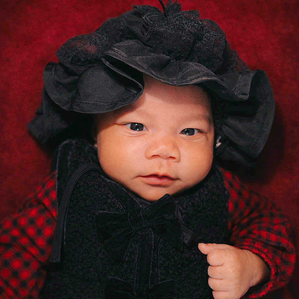 Hara-Mia joined the competition — help win amazing prizes! baby, black_hat, black_vest, bow, child, closeup, cute, expression, face, fist, hand, hat, indoor, infant, looking_at_camera, portrait, red_background, red_checkered_clothing, vest, young