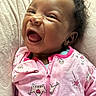 baby, child, smiling, laughing, pink_clothing, onesie, crown_pattern, cute, happy, infant, face, head, curly_hair, soft_blanket, texture, portrait, closeup, person, indoors, cozy