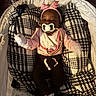 baby, infant, pacifier, blanket, crib, headband, bow, pink_clothing, black_pants, mittens, footwear, plush, patterned_blanket, cushion, sleeping_area, indoor, child, portrait, cozy, soft_lighting