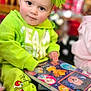 child, toddler, green_clothing, book, reading, headband, bow, indoor, cute, holiday_theme, face, eyes, sitting, floor, toy, colorful, expression, person, young_child, playful