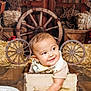 baby, child, smiling, wooden_box, barn, wagon_wheel, string_lights, hay, meat, plate, floor, scarf, cute, indoor, rustic, decor, wood, happy, infant, portrait