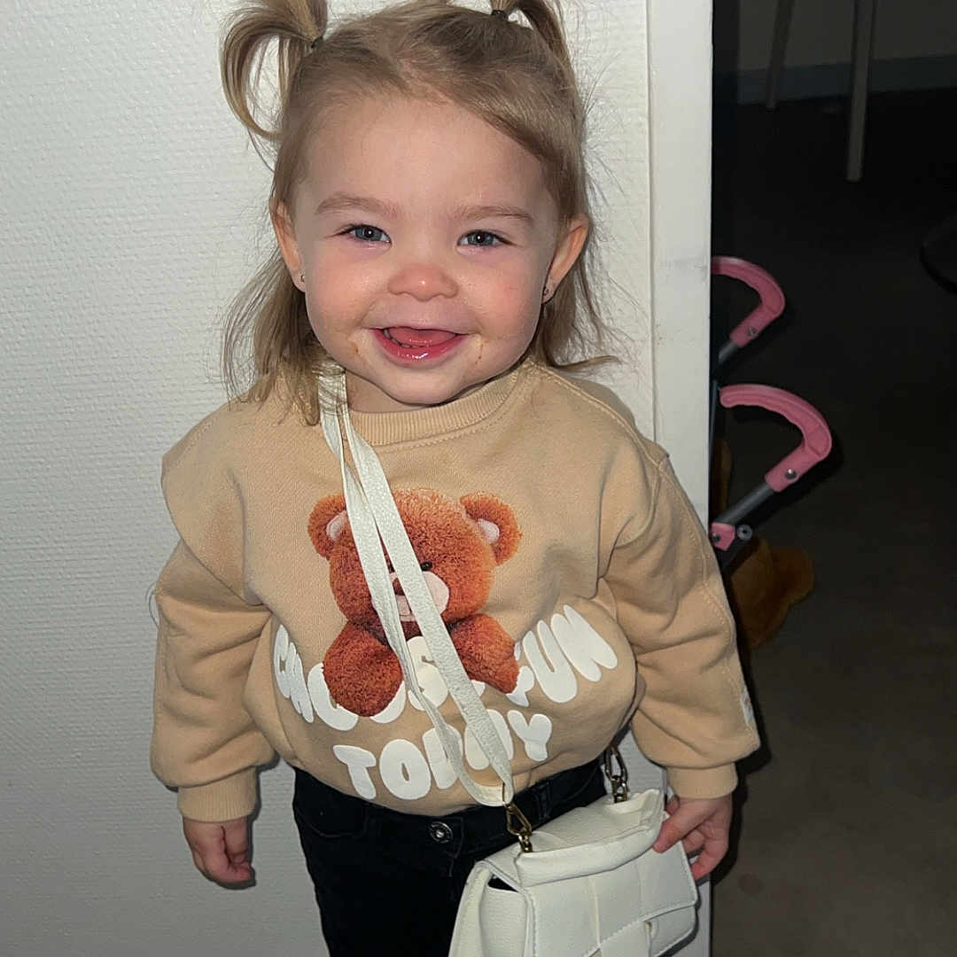 Cheryl a rejoint le concours — aidez-le/la à gagner de superbes lots ! toddler, child, smiling, indoor, pigtails, sweatshirt, teddy_bear, white_purse, black_pants, white_sneakers, floor, wall, doorway, stroller, furniture, happy, cute, person, portrait, fashion