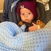 Michael joined the competition — help win amazing prizes! baby, infant, car_seat, blanket, hat, child, indoor, clothing, person, face, expression, warm, cozy, seated, blue, maroon, yellow, cute, small_hand, looking