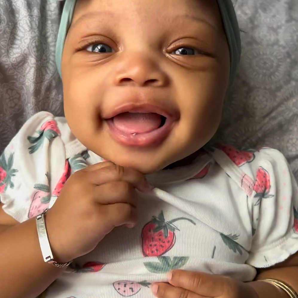 Sevynn is registered to the contest to win money with this photo: baby, bow, bracelet, child, closeup, cute, face, hand, happy, headband, infant, jewelry, lying_down, onesie, pattern, pillow, portrait, smiling, soft_lighting, strawberry_print