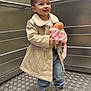 beige_coat, boots, casual_clothing, child, cute, doll, elevator, floor_pattern, happy, holding, indoor, jeans, metal_wall, person, play, portrait, smiling, standing, toy, young_child