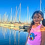 Nelya participe au concours pour gagner de l'argent avec cette photo : blue_sky, cartoon_character, casual, child, girl, happy, harbor, marina, outdoor, person, pigtails, reflection, rocks, sailboats, shadows, smile, summer, sunlight, tank_top, water