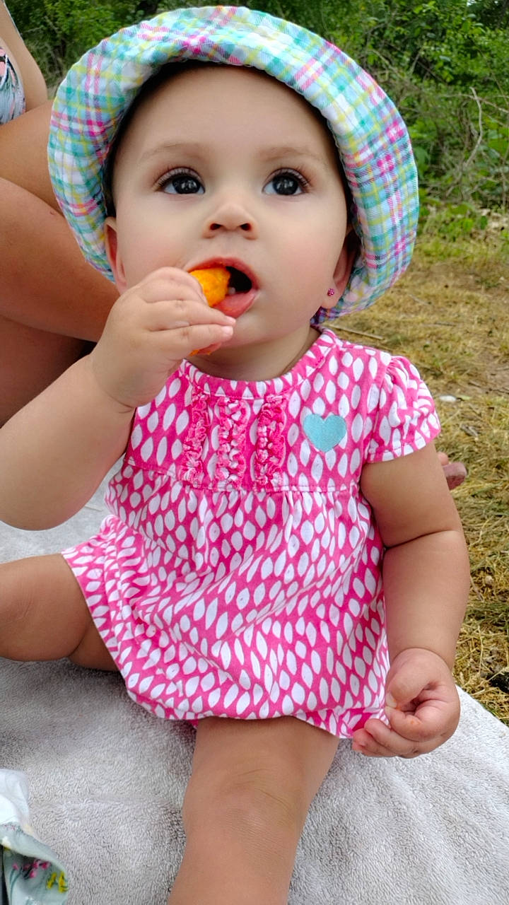 Azaria is registered to the contest to win money with this photo: baby_toddler_clothing, cheek, child, chin, dress, finger, fruit, happy, hat, headwear, lip, mouth, neck, nose, person, pink, plant, skin, sleeve, summer