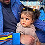 child, man, pigtails, hair_clips, blue_jacket, striped_sleeve, amusement_ride, colorful_lights, playful_background, outdoor, cute, family, portrait, people, clothing, holding, face, expression, fun, daytime