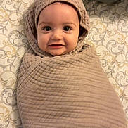 Finnley is registered to the contest to win money with this photo: baby, blanket, wrapped, smiling, face, bed, patterned_bedspread, soft_lighting, indoors, cute, child, cozy, head, infant, person, portrait, skin, happy, lying_down, warm