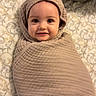 baby, blanket, wrapped, smiling, face, bed, patterned_bedspread, soft_lighting, indoors, cute, child, cozy, head, infant, person, portrait, skin, happy, lying_down, warm