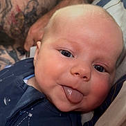 Rosey is registered to the contest to win money with this photo: baby, infant, tongue_out, face, blue_eyes, tattoos, adult, skin, necklace, clothing, striped_sleeve, close_up, portrait, cute, expression, person, indoor, comfort, holding, smile
