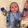 baby, infant, crocheted_jacket, blue_onesie, shark_pattern, pacifier, quilted_blanket, lying_down, wide_eyes, curious, cute, colorful_clothing, knitwear, soft_texture, indoors, child, newborn, baby_clothes, portrait, stillness