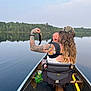 tattoo, adult, baby, canoe, lake, fish, crying, water, forest, nature, outdoor, person, hat, long_hair, paddle, seat, can_holder, drink_can, reflection, sky