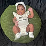baby, infant, headband, white_clothing, socks, green_cushion, knitted, raised_arm, black_background, cute, child, portrait, indoor, sitting, looking_at_camera, one_person, closeup, soft_lighting, expression, newborn