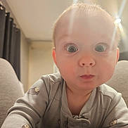 Elijah is registered to the contest to win money with this photo: baby, child, face, wide_eyes, curious, indoors, pajamas, soft_lighting, close_up, portrait, expression, human, infant, cute, young, person, room, blurred_background, sitting, candid