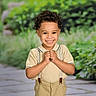 child, boy, smiling, curly_hair, suspenders, short_sleeve_shirt, outdoor, portrait, happy, greenery, pathway, cute, young, fashion, casual, person, nature, background_blur, standing, light