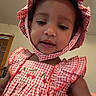 child, toddler, dress, bonnet, red_and_white, gingham, indoor, smiling, face, cute, person, window, wall, headwear, clothing, portrait, young_child, baby, happy, girl
