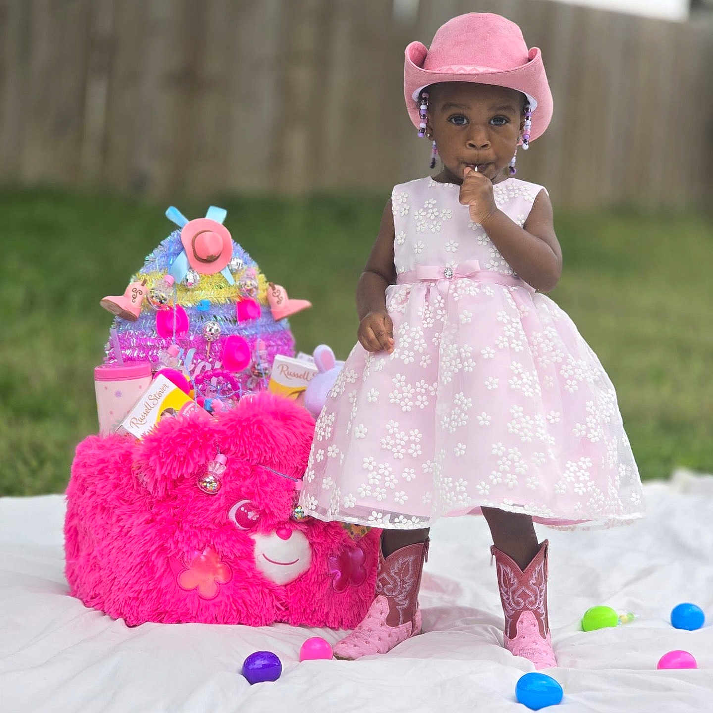 J Zelle joined the competition — help win amazing prizes! beads, child, colorful_eggs, cowboy_boots, cowboy_hat, cute, grass, outdoor, pink_bear, pink_dress, playful, plush_toy, portrait, ribbons, standing, sucking_thumb, toddler, toy_basket, white_blanket, wooden_fence