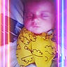Caroline is registered to the contest to win money with this photo: baby, sleeping, yellow_clothing, neon_lights, glowing_frame, portrait, infant, cute, peaceful, indoors, child, soft_lighting, colorful, patterned_clothes, neon_effect, face, resting, young_child, blanket, cozy