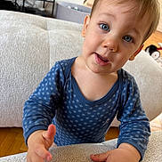 Marceau participe au concours pour gagner de l'argent avec cette photo : toddler, child, blue_onesie, polka_dots, curious, indoor, couch, hand, face, portrait, young_child, expression, eyes, skin, hair, home, furniture, floor, person, baby