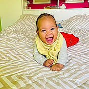 Naïann participe au concours pour gagner de l'argent avec cette photo : baby, bed, bedding, blanket, child, comforter, face, furniture, happy, indoor, infant, person, portrait, red_pants, smiling, yellow_bib, young_child, photography, room, wall