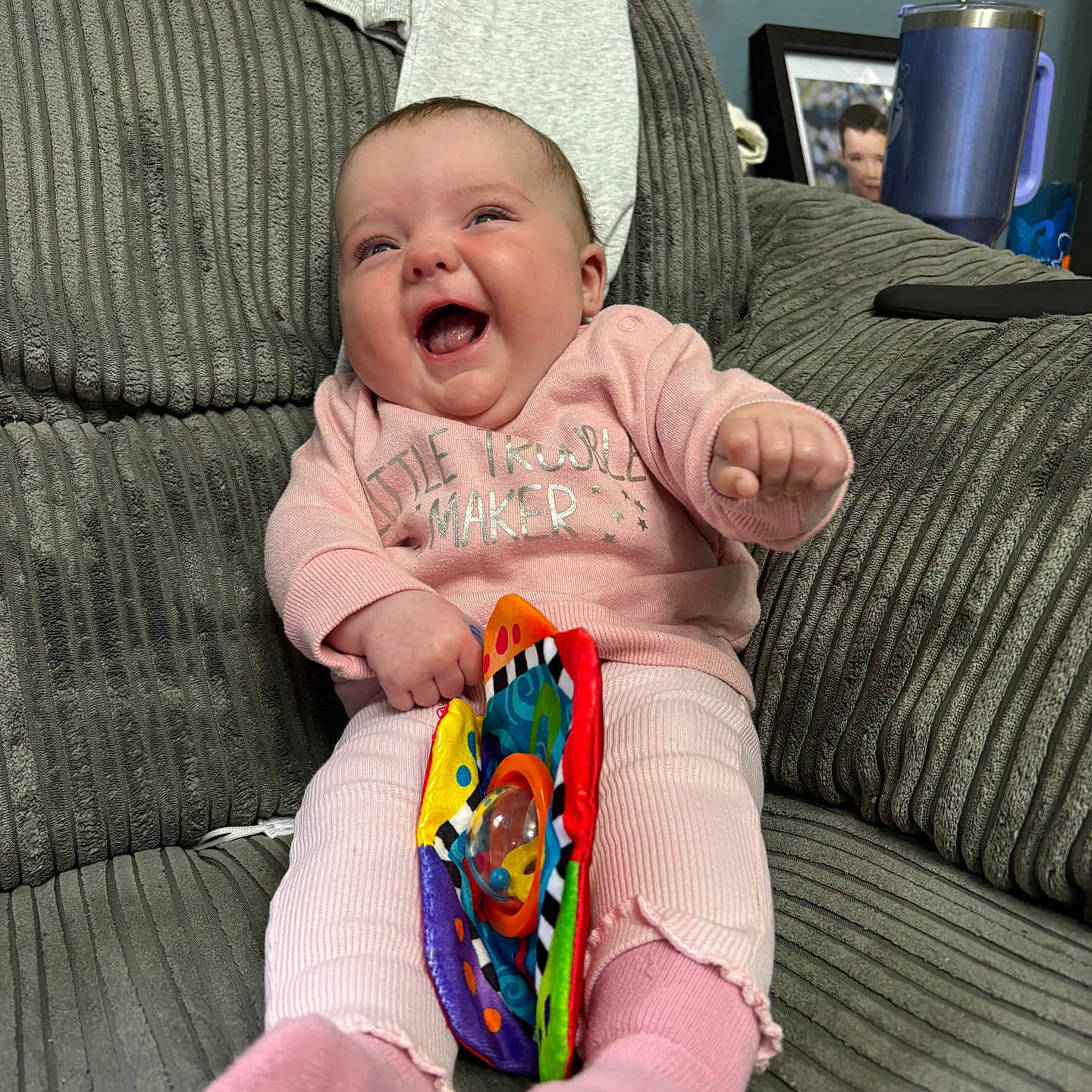 Remy-Beaux is registered to the contest to win money with this photo: baby, child, colorful_toy, couch, cozy, cute, furniture, gray_fabric, happy, home, indoor, infant, pajamas, pink_clothing, playful, portrait, sitting, smiling, soft_toy, toy