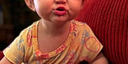 Cadence is registered to the contest to win money with this photo: toddler, child, face, expression, pout, couch, red_couch, hand, clothing, patterned_clothing, indoors, person, cute, baby, seated, skin, furniture, home, funny_face, young_child