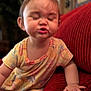 toddler, child, face, expression, pout, couch, red_couch, hand, clothing, patterned_clothing, indoors, person, cute, baby, seated, skin, furniture, home, funny_face, young_child