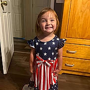 Paisley joined the competition — help win amazing prizes! barefoot, blanket, bow, child, clothing, cute, door, dress, floor, girl, happy, home, indoor, person, portrait, smile, standing, stars, stripes, wooden_furniture