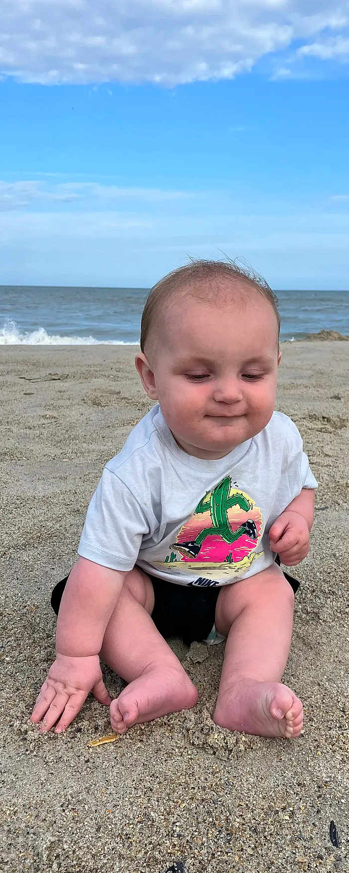 Anthony joined the competition — help win amazing prizes! baby, child, beach, sand, ocean, waves, tshirt, cactus_graphic, sitting, barefoot, cute, smiling, outdoor, sky, clouds, summer, playful, young, person, natural_light