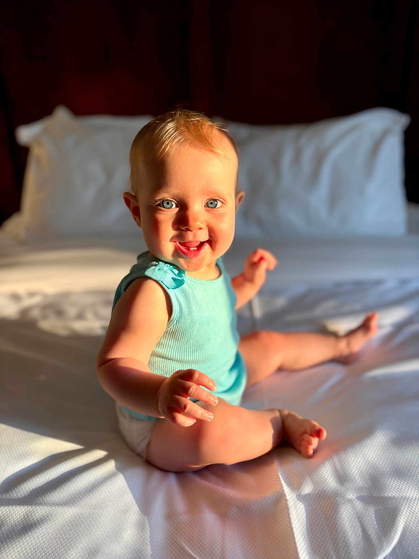 Finnley is registered to the contest to win money with this photo: baby, child, infant, smiling, blue_eyes, sitting, bed, white_sheet, sunlight, shadow, turquoise_top, cute, happy, indoor, portrait, skin, hand, foot, expression, person