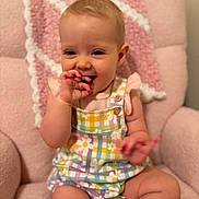 Finnley is registered to the contest to win money with this photo: baby, child, infant, smiling, sitting, pink_chair, colorful_clothing, romper, hand, face, cute, happy, indoors, soft_texture, blanket, patterned_clothing, young_child, playful, fingers, portrait