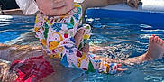 Finnley joined the competition — help win amazing prizes! adult_hand, baby, blue, child, colorful_clothing, cute, nature, outdoor, person, pool, recreation, reflection, smile, summer, sunhat, sunlight, swimsuit, trees, water, water_surface