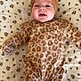 baby, infant, smiling, face, headband, leopard_print, onesie, clothing, lying_down, blanket, floral_pattern, cute, child, happy, portrait, indoors, small_child, soft_fabric, baby_wear, toddler