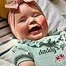 Emilia is registered to the contest to win money with this photo: baby, smiling, girl, headband, bow, clothing, mint_green, rosy_cheeks, closeup, portrait, infant, happy, cute, soft_lighting, fabric, text_on_clothing, lying_down, indoor, child, face
