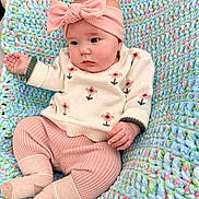 Emilia is registered to the contest to win money with this photo: baby, infant, child, knitted_blanket, pink_bow, headband, sweater, floral_pattern, pink_pants, cozy, cute, soft_texture, pastel_colors, portrait, indoors, candid, small_hands, socks, seated, comfortable